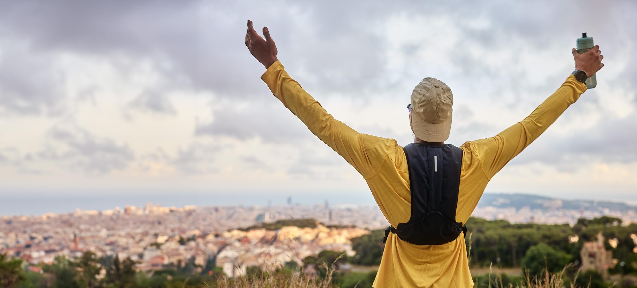 Man overlooking a city from a mountain, holding his arts in the air and a BRITA Active bottle