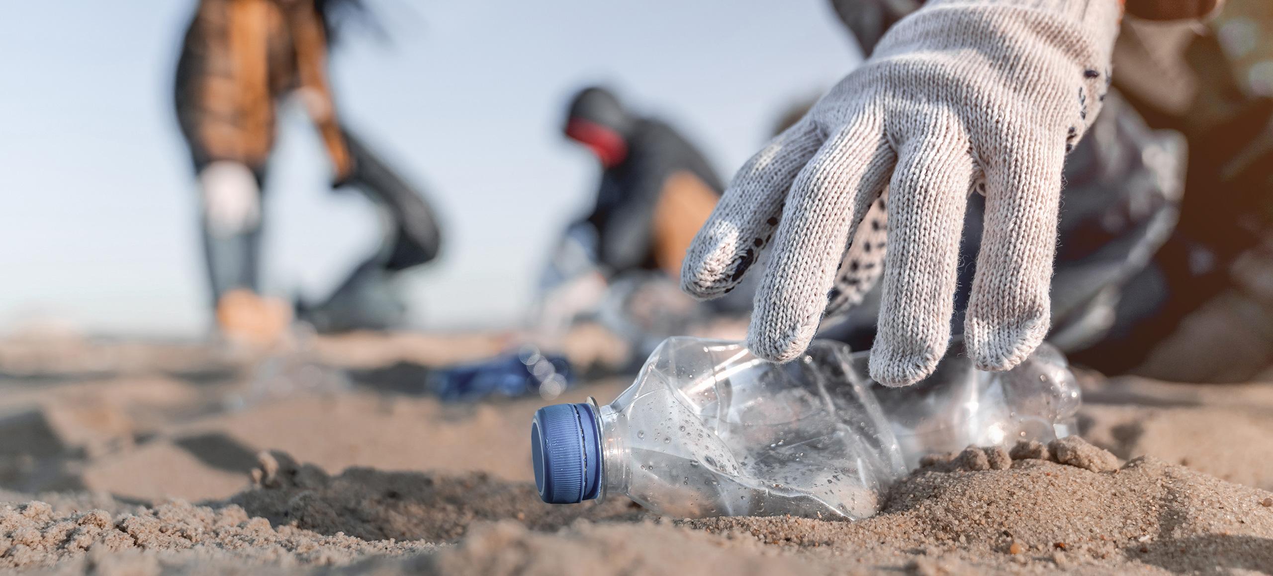 People at a beach clean where a person is picking up a single-use plastic bottle