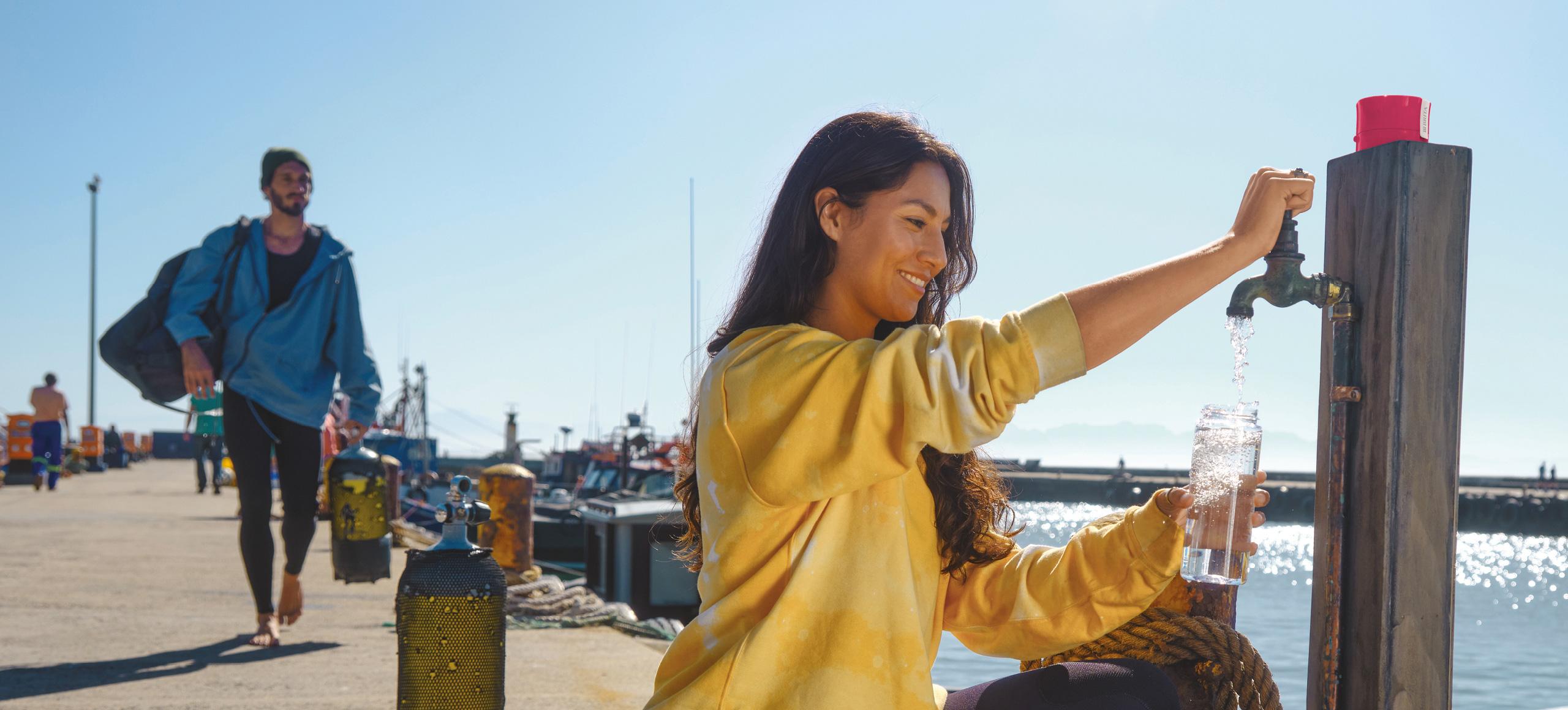 Woman filling up reusable BRITA Water Filter bottle from a tap outdoors.