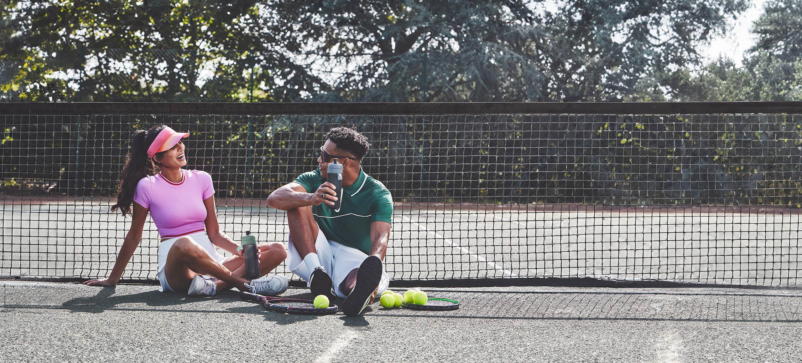 A woman and man sat on a tennis court with BRITA Active Water Filter bottles